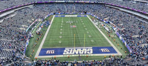 Ein volles Fußballstadion mit Spielern auf dem Feld, Torpfosten und Texttafeln, von oben während eines Spiels betrachtet.
