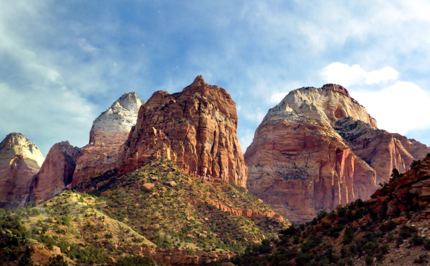 Ein malerischer Blick auf den Zion-Nationalpark in Utah mit majestätischen Bergen, grünen Bäumen, felsigem Gelände und einem Himmel mit weißen Wolken.