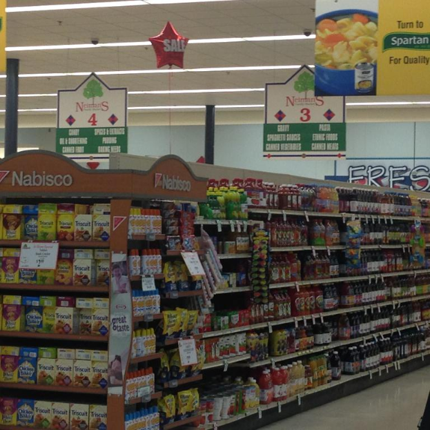 Ein Supermarkt-Innenraum mit sichtbaren Lebensmitteln, Deckenlampen und hängenden Schildern.