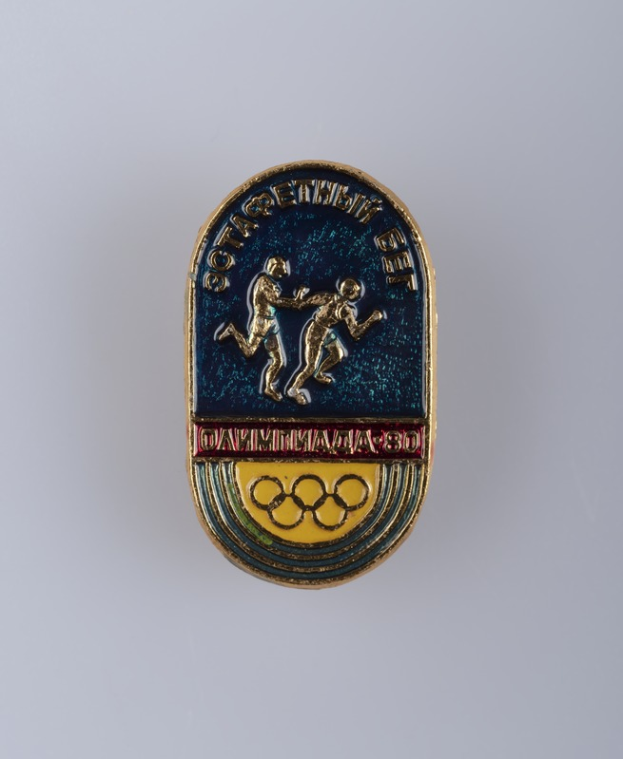 Ein runder Abzeichen mit dem Logo der Olympischen Spiele 1980 in Moskau, das zwei Läufer und den Text 'Olympische Spiele' darüber zeigt.