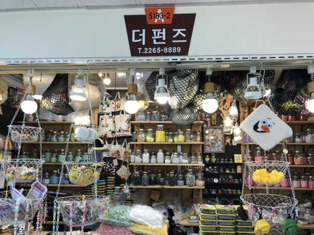 Ein unordentlicher Ladeneinrichtungsdisplay in Seoul mit Körben, Lichtern, Flaschen, Spielzeugen und anderen Artikeln auf Regalen, mit einer Tafel oben, die anzeigt, dass es eines der besten koreanischen Geschäfte ist.