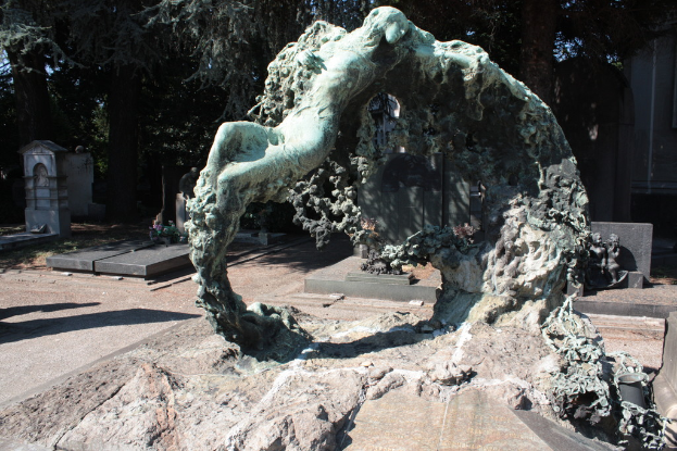 Ein Friedhof mit zahlreichen Gräbern, umgeben von vielen Bäumen und einer Skulptur im Vordergrund.