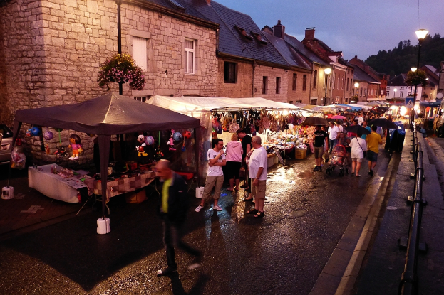 Eine Gruppe von Menschen auf einer Straße mit Geschäften, Schirmen, hängenden Spielzeugen, Taschen, Gebäuden mit Fenstern, Bäumen, Straßenlaternen und Barrikaden.