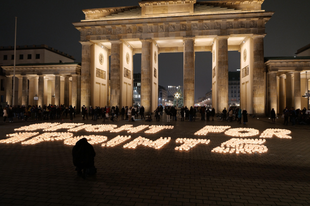 Eine Gruppe von Menschen steht vor dem beleuchteten Brandenburgertor in Berlin, Deutschland, umgeben von Gebäuden, Masten und Lichtern, mit den Worten "Kampf für die Freiheit" auf dem Boden geschrieben.