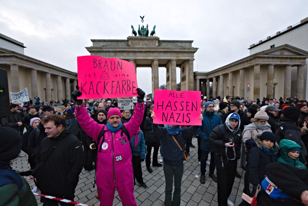 Gruppe von Menschen demonstriert vor dem Brandenburger Tor in Berlin, hält Schilder gegen die anti-nazistische Bewegung der deutschen Regierung, mit Gebäuden und Statuen im Hintergrund unter einem klaren blauen Himmel.