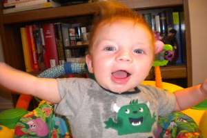 Ein Kind sitzt auf einem Stuhl vor einem teilweise sichtbaren Bücherregal mit Büchern, vor einem abgeschnittenen Wandhintergrund.