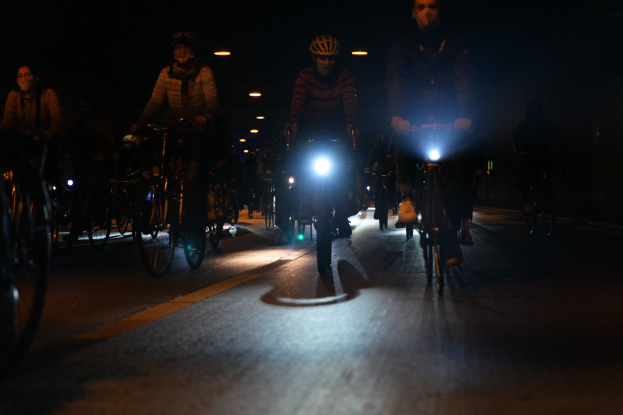 Eine Gruppe von Menschen, die nachts auf Fahrrädern durch eine Stadtstraße fahren, Helme tragen und von Stadtlichtern beleuchtet werden.
