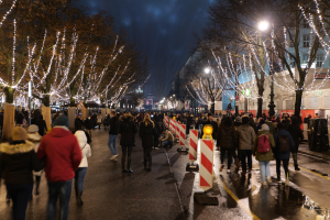 Eine Menschenmenge, die nachts eine Straße entlanggeht, mit beleuchteten Bäumen und Gebäuden.