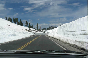 Eine Aufnahme aus einem Fahrzeug, die eine leere Straße, schneebedeckte Berge und Bäume daneben zeigt.