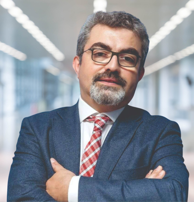 Ein Mann in Anzug und Krawatte mit verschränkten Armen und Brille steht vor einem unscharfen Hintergrund mit Text, der ihn als neu ernannten Marketingchef identifiziert.