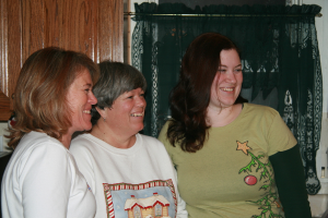 Frauen vor einer Wand mit grünem Vorhang und einem hölzernen Fenster lachend