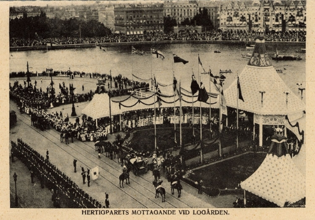 Ein altes Schwarz-Weiß-Foto einer Menge, die sich um einen Karneval mit Zelten, Fahnen, Stangen und Pferden im Vordergrund versammelt hat, und Gebäude, Bäume und Wasser im Hintergrund, mit Text am unteren Rand des Bildes.