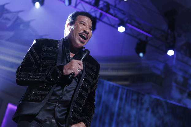 Lionel Richie performs bei den Grammys, tr├Ągt einen schwarzen Anzug und h├Ąlt ein Mikrofon auf einer hell erleuchteten Bühne.