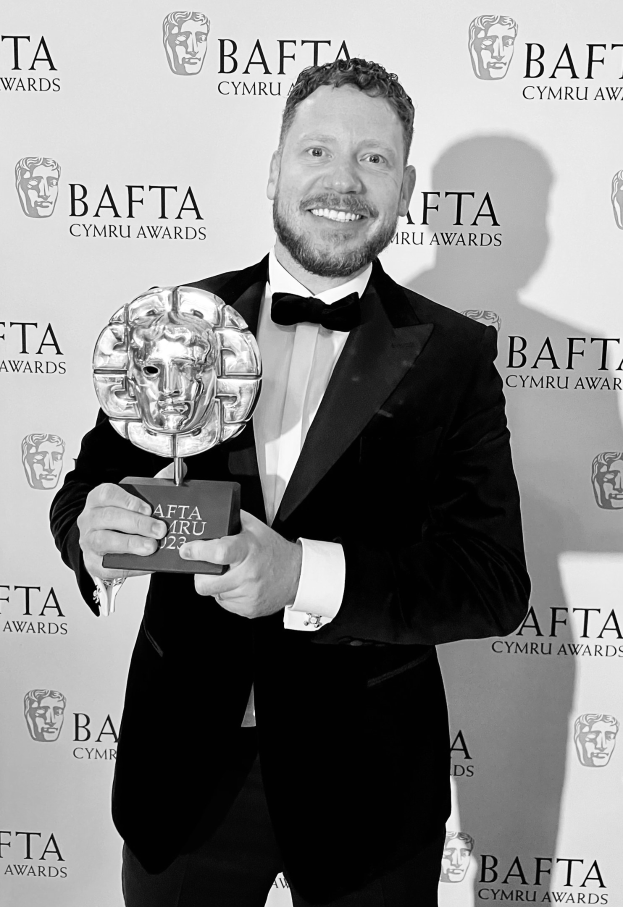 Ein Mann in einem Smoking, der eine BAFTA-Trophäe hält und lächelt, mit einem Hintergrund, auf dem "BAFTA Awards 2018" steht.