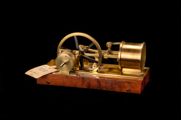 Altmodische Uhr mit einem hölzernen Sockel, Metallrad und einem daran befestigten Papier, vor einem schwarzen Hintergrund, möglicherweise als Zeitumschalter fungierend.