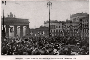 Eine große Menschenmenge in Hüten und einige mit Fahnen vor dem Brandenburger Tor in Berlin, Deutschland, 1918, mit den Säulen und Statuen des Tors im Hintergrund.