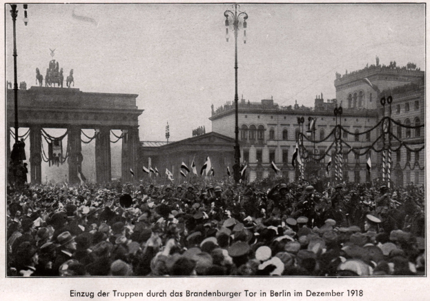 Eine große Menschenmenge in Hüten und einige mit Fahnen vor dem Brandenburger Tor in Berlin, Deutschland, 1918, mit den Säulen und Statuen des Tors im Hintergrund.