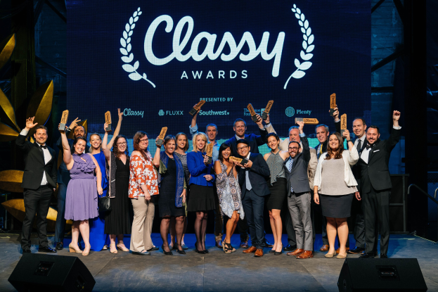 Gruppe von Menschen auf einer Bühne mit Auszeichnungen, mit Lautsprechern darunter und einem Bildschirm, der "Classy Awards 2019" anzeigt.