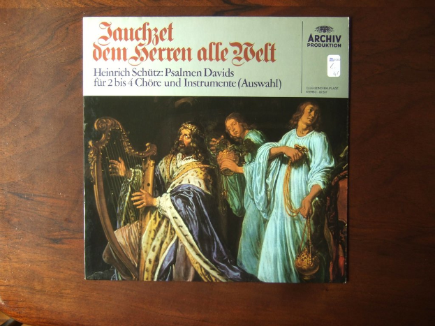 Ein Buch mit einem Namen darauf wird auf einen Holztisch gestellt, mit Menschen im Hintergrund, die Musikinstrumente spielen.