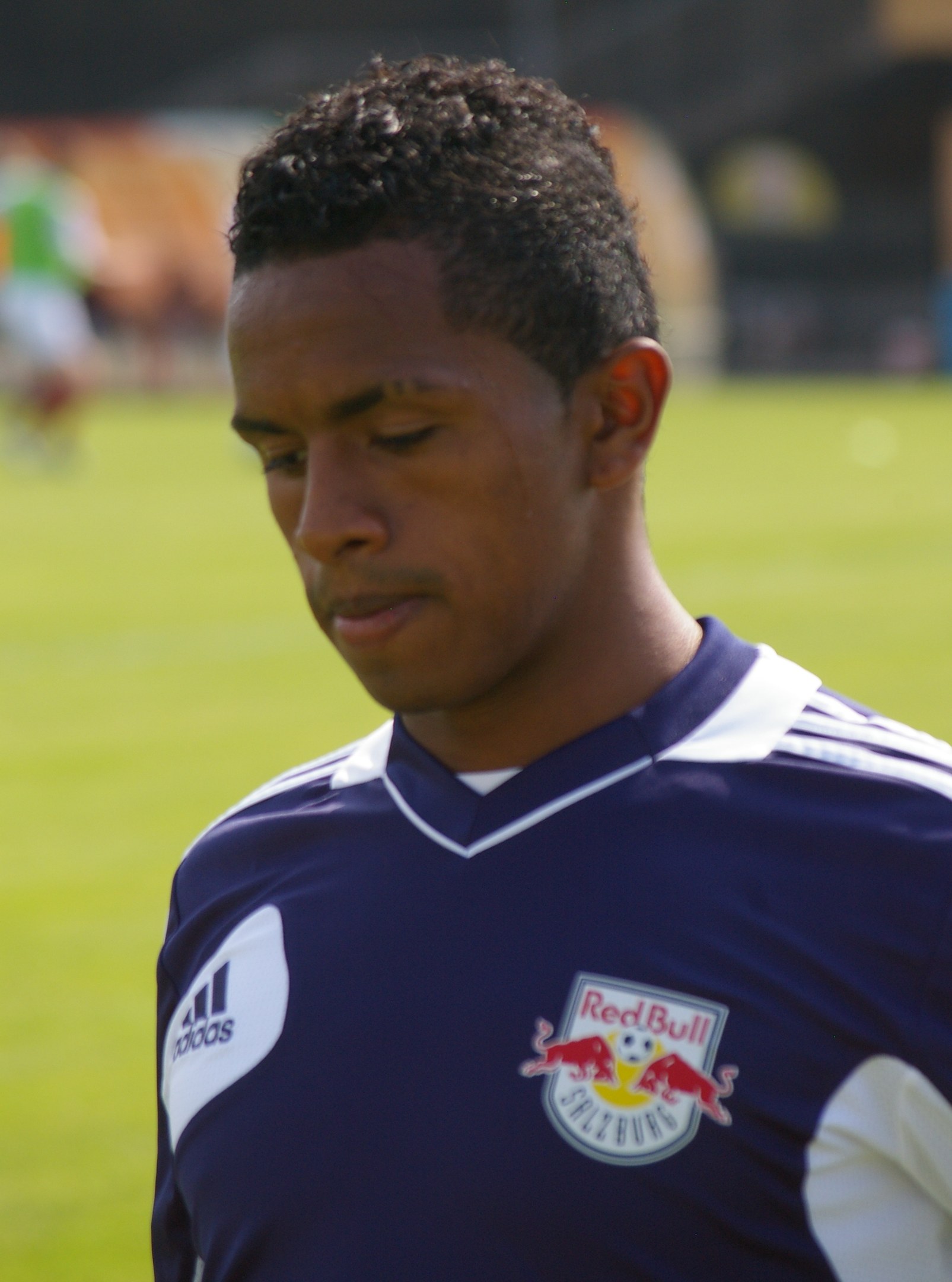 Junger Mann in einem blauen T-Shirt auf einem Fußballfeld, der als Flügelspieler mit kurzen dunklen Haaren und einem entschlossenen Gesichtsausdruck erscheint.
