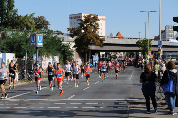 Gruppe von Menschen beim Marathonlauf auf einer von Bäumen gesäumten Straße unter einem klaren blauen Himmel.