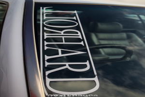 Windschutzscheibe eines Autos mit Text, durch die Scheibe sind Lenkrad und Sitze zu sehen.