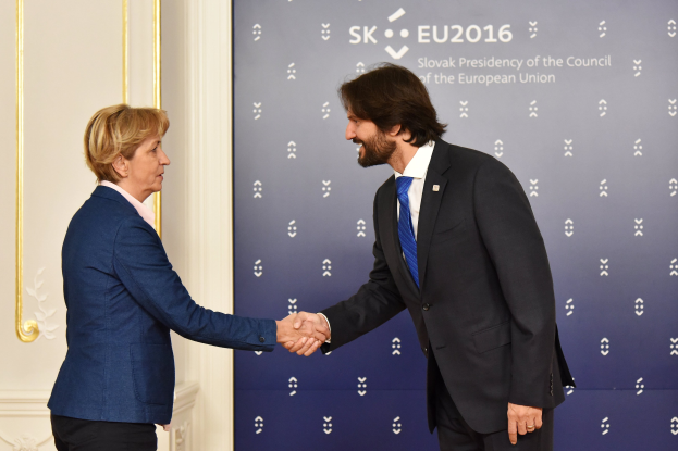 Bundeskanzlerin Angela Merkel und Bundeskanzler Joachim Gauck schütteln sich vor einer Wand mit einem "EU-Gipfel"-Banner und einer Tür im Hintergrund die Hand, beide lächeln.