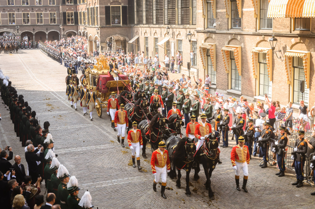 Eine Gruppe von Menschen, die auf Pferden eine Straße entlangreiten, neben einer Menge mit Kameras und Mobiltelefonen, mit Gebäuden und Laternen im Hintergrund, während der Krönung von König Willem-Alexander und Königin Maxima der Niederlande.