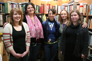 Eine Gruppe von Menschen, einer trägt eine Brille, mit Bücherregalen im Hintergrund.