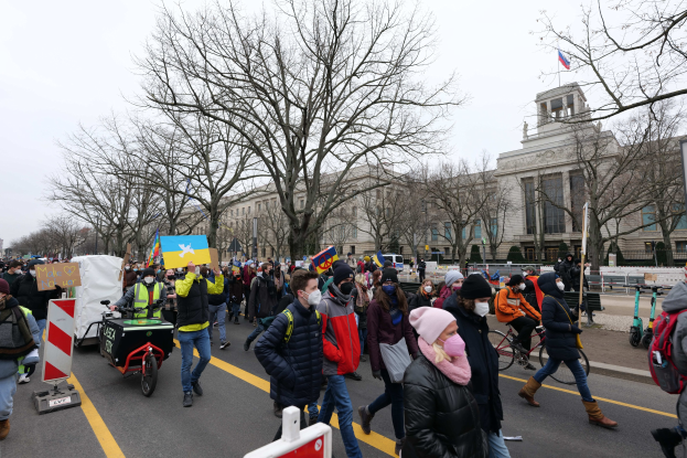 Großer Protestmarsch in Washington, D.C. am 21. Januar 2020 mit Menschen, die die Straße vor einem Gebäude entlanggehen, Schilder halten und Fahrräder fahren, unter einem klaren blauen Himmel.