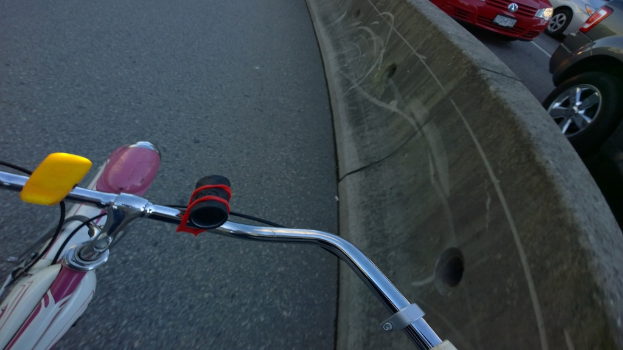 Ein Fahrradlenker befindet sich unten im Bild, mit Fahrzeugen, die sich auf der rechten Seite auf der Straße bewegen, und einer Trennung in der Mitte.