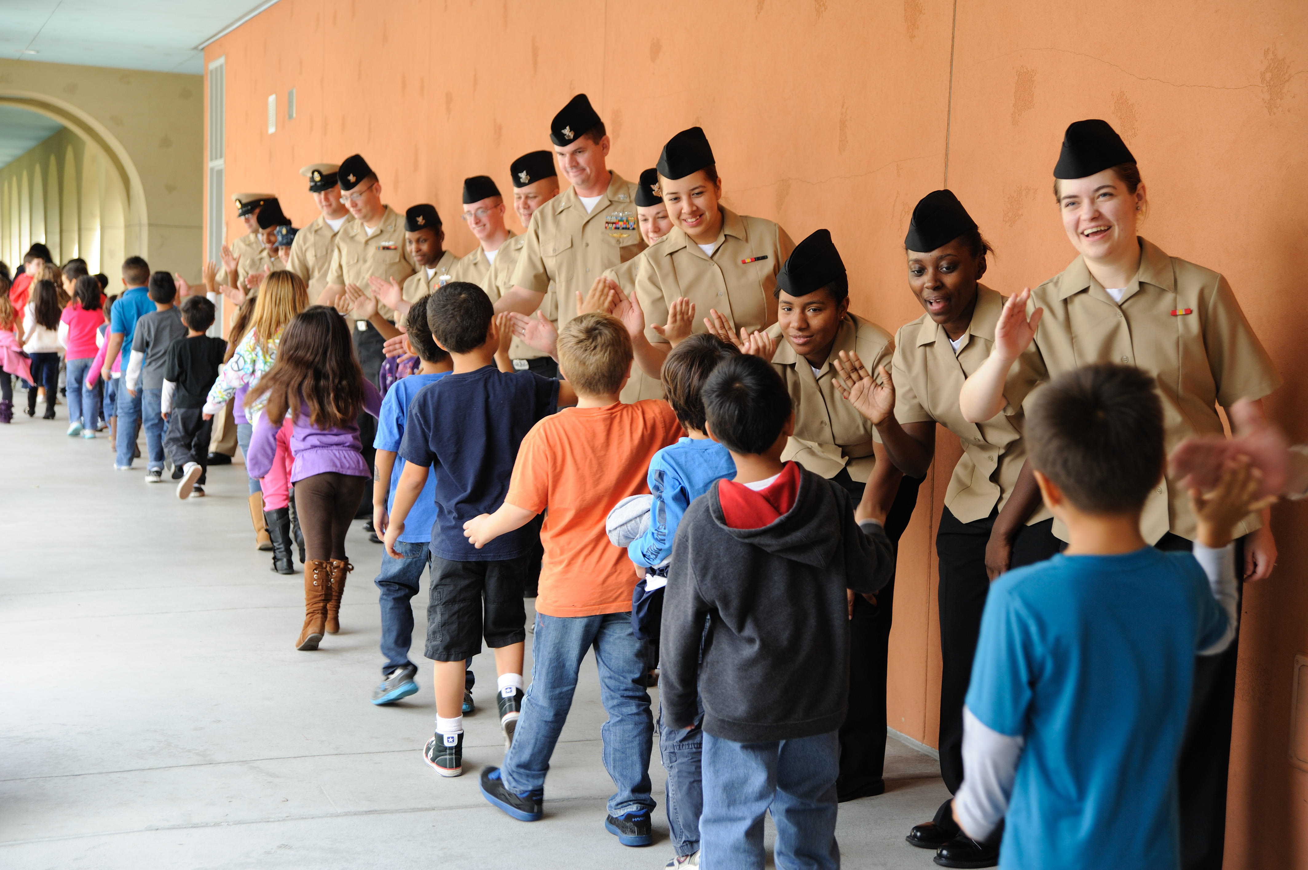 Eine Gruppe von Kindern in Uniformen, die einen Flur entlanggehen, mit einer Wand auf der rechten Seite und einer Decke mit Lampen oben.