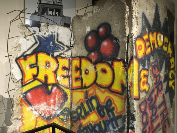 Mauer mit Graffiti, das in fetten schwarzen Buchstaben "Freiheit und Demokratie" lautet, ein Geländer unten und ein Gebäude mit Fenstern im Hintergrund.