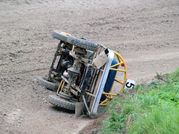 Ein Auto liegt auf der Seite auf einer Schotterstraße mit Gras auf der rechten Seite.