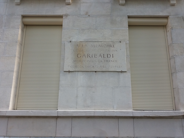 Ein Gebäude mit zwei Fenstern und Läden, das eine Gedenktafel an seiner Außenwand trägt.