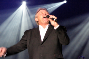 Ein Mann mit Mikrofon auf der Bühne mit Scheinwerfern im Hintergrund.