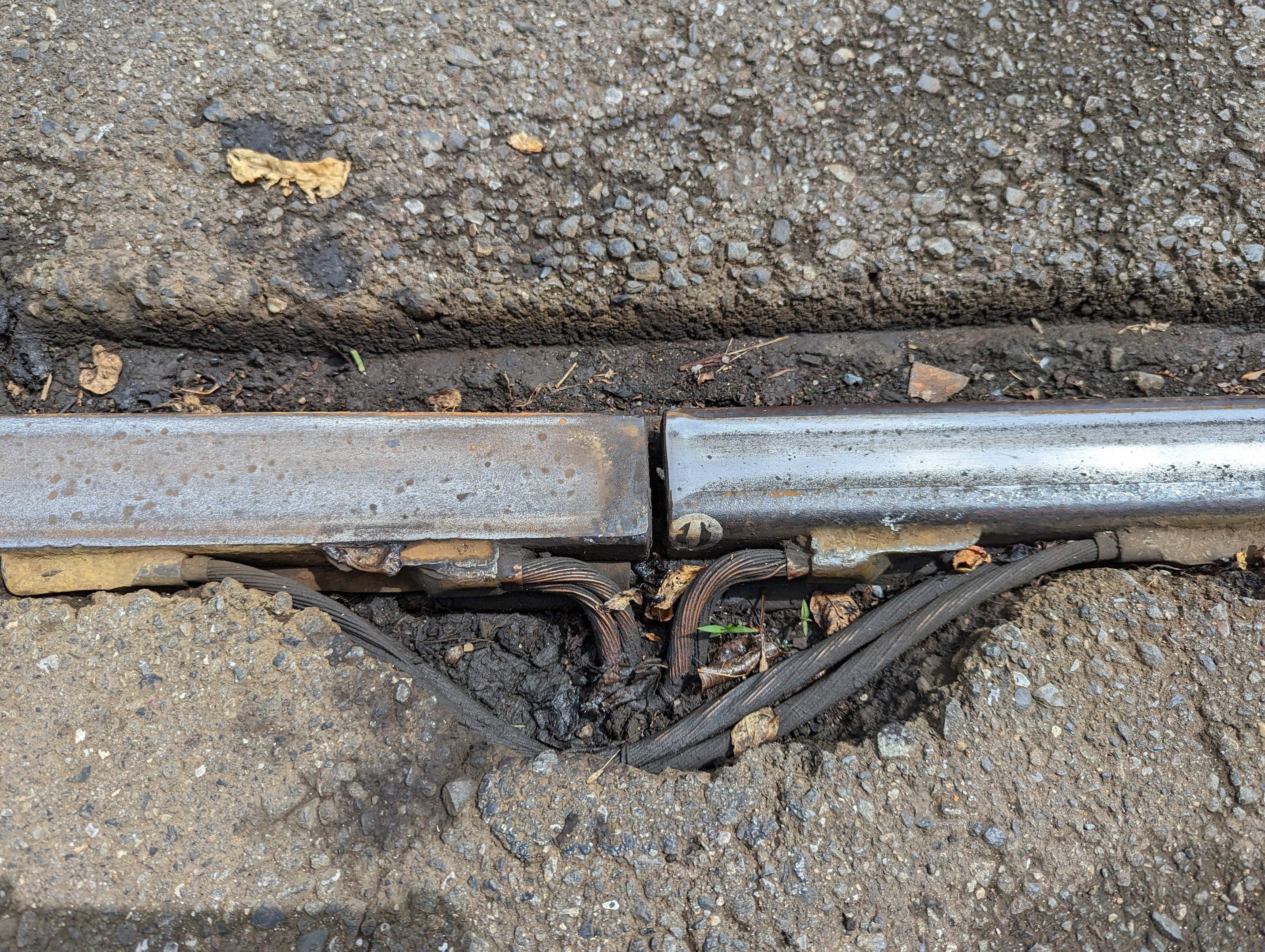 Nahaufnahme eines Metallkanalrohrs auf einem Straßenrand mit verstreuten Drähten und trockenen Blättern, verbunden mit dem Boden.