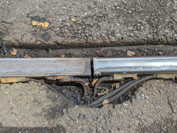 Nahaufnahme eines Metallkanalrohrs auf einem Straßenrand mit verstreuten Drähten und trockenen Blättern, verbunden mit dem Boden.