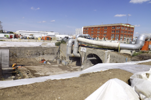 Eine Szene mit Gebäuden, einem Zaun, Fahrzeugen, aktuellen Umfragen, einer Leitung und dem Himmel darüber.