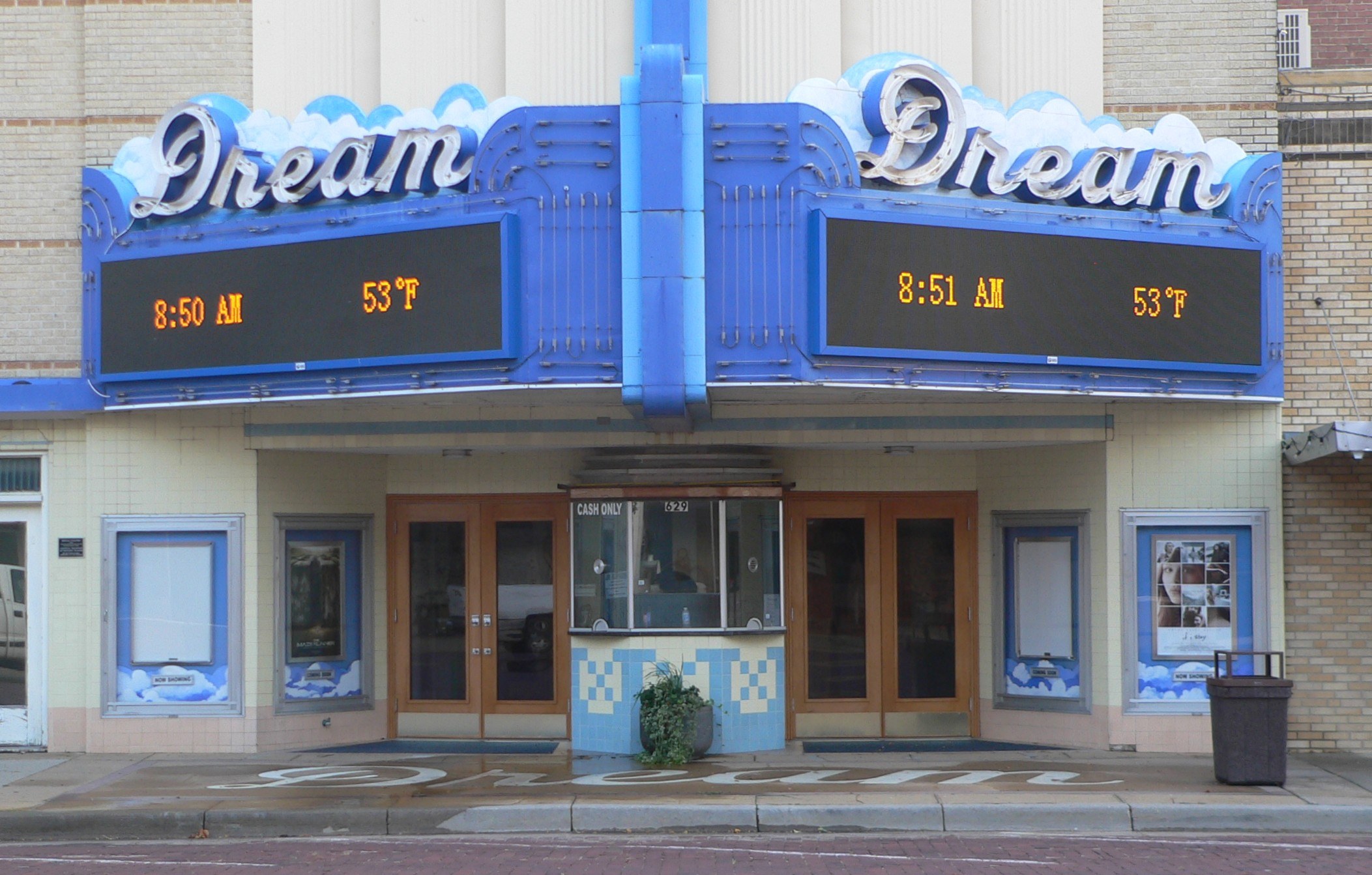 Außenansicht des Dream Theaters in St. Louis, Missouri, mit Glastüren und -fenstern, einem Namensschild, einem Müllcontainer, einem Topf mit einer Pflanze und einer Straße unten.