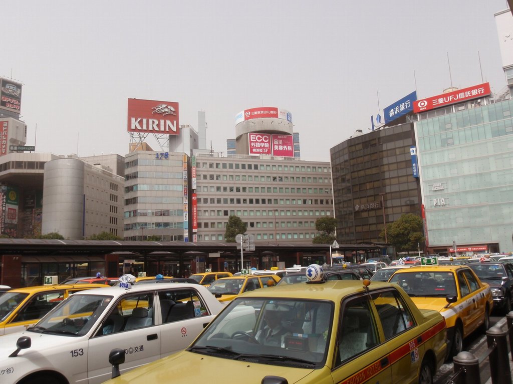 Eine Stadtansicht mit Fahrzeugen auf der Straße, Gebäuden, Bäumen, Polen mit Schildern und Text auf den Schildern, einem Zug im Hintergrund und einem Geländer unten rechts.