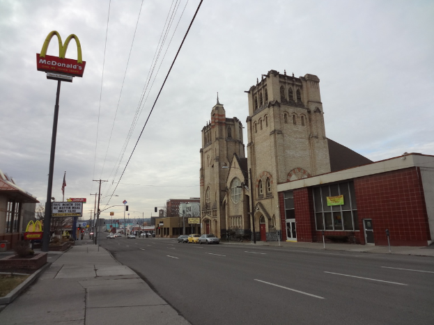 Eine Straßenansicht mit Gebäuden auf der rechten Seite, Pfählen und Autos in der Mitte und einem McDonald's-Schild auf der linken Seite.