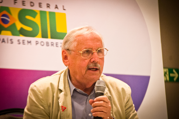 Eine Person, die in ein Mikrofon spricht und von einem Banner mit der Aufschrift 'Bundes' hinter ihr flankiert wird.