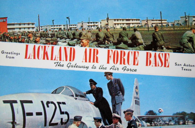 Eine Gruppe uniformierter Personen steht vor einem Flugzeug auf der Lackland Air Force Base, mit Gebäuden, Polen, Bäumen und einem klaren blauen Himmel im Hintergrund.