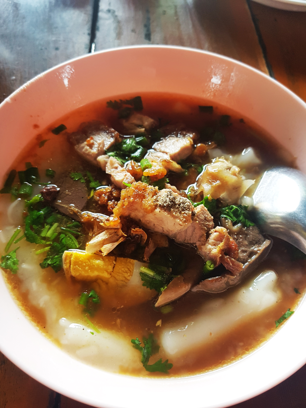 Eine Schüssel dampfender Suppe mit Fleisch und Gemüse, mit einem Löffel, der an ihrer Seite ruht.