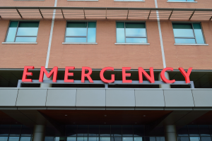 Ein Gebäude mit Glasfenstern, Säulen und einem sichtbaren roten Notfallzeichen, das darauf hinweist, dass es eine Notaufnahme ist.