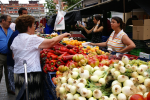 Eine Gruppe von Menschen, die sich draußen in der Nähe von Gebäuden und Bäumen aufhalten, mit Gemüse in Plastikbehältern und einer Kartonschachtel.