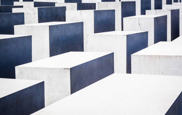 Eine große Anzahl rechteckiger Betonplatten in verschiedenen Höhen, die in einem Gittermuster auf einem geneigten Feld angeordnet sind, bekannt als Holocaust-Mahnmal für die ermordeten Juden Europas in Berlin, Deutschland.