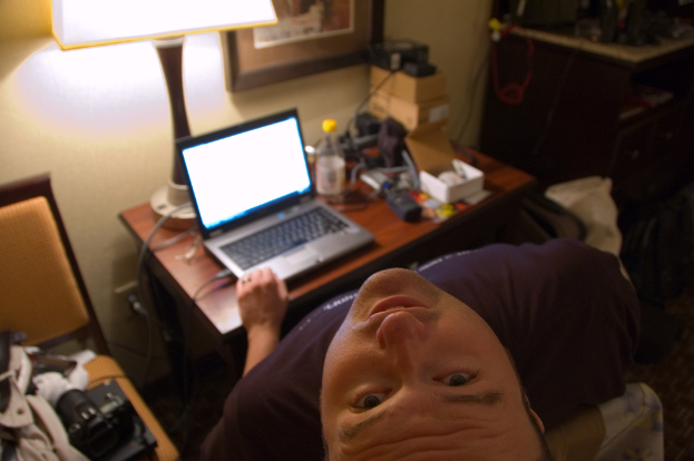 Eine Person, die in einem Stuhl sitzt und auf einem Laptop arbeitet, mit einer Lampe vor sich und den Kopf nach oben geneigt.