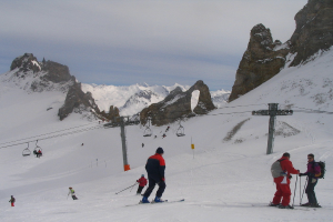 Menschen in Pullovern fahren Ski auf dem Eis, mit einer Seilbahn, Bergen und einem bewölkten Himmel im Hintergrund.